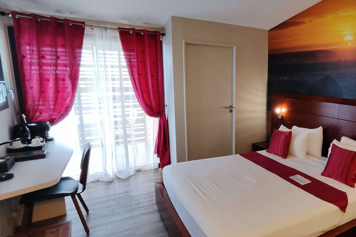 A hotel room with a bed, desk, chair, and a painting on the wall.