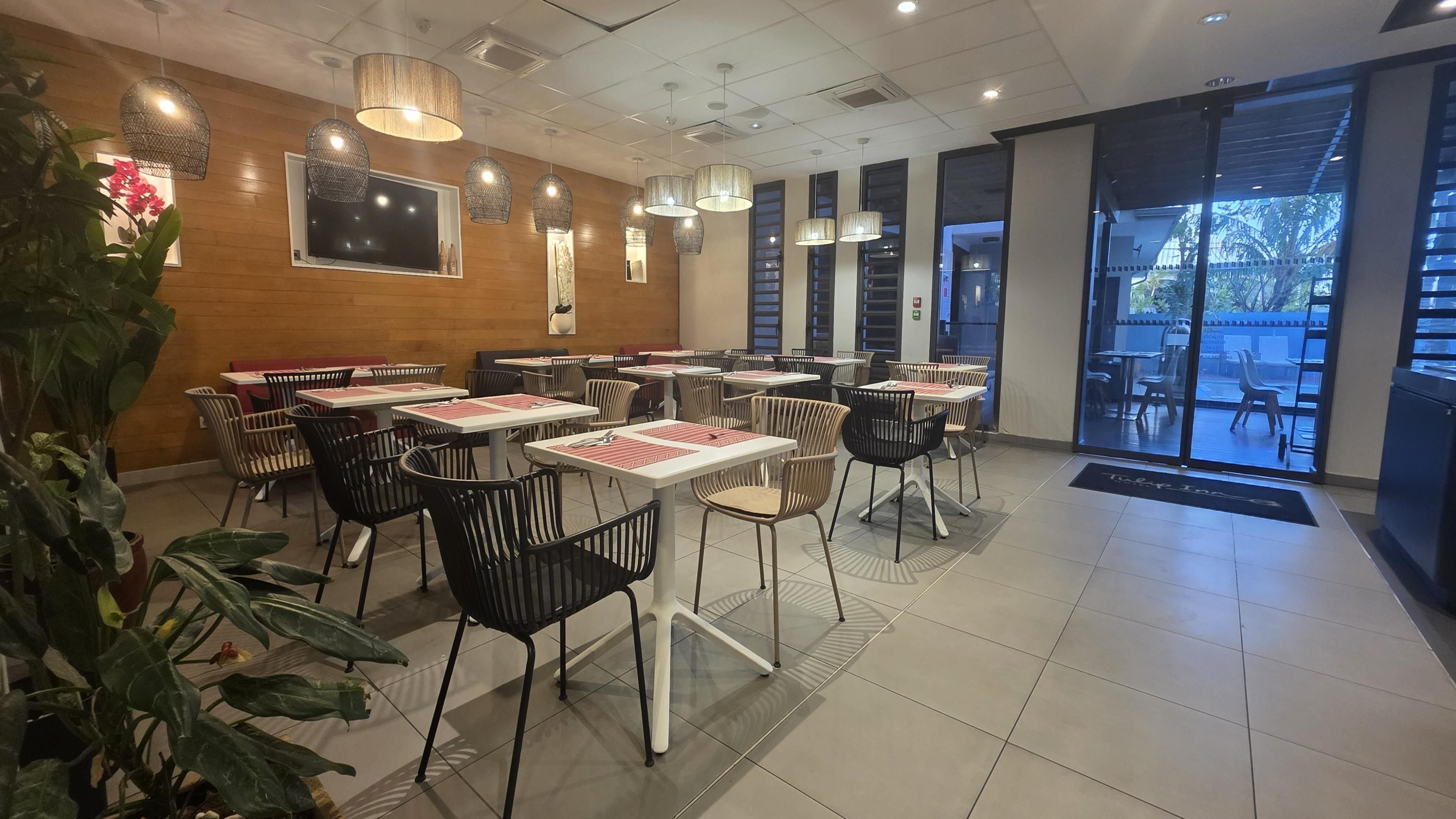 Interior de restaurante con mesas, sillas, una pantalla de televisión y luces colgantes.