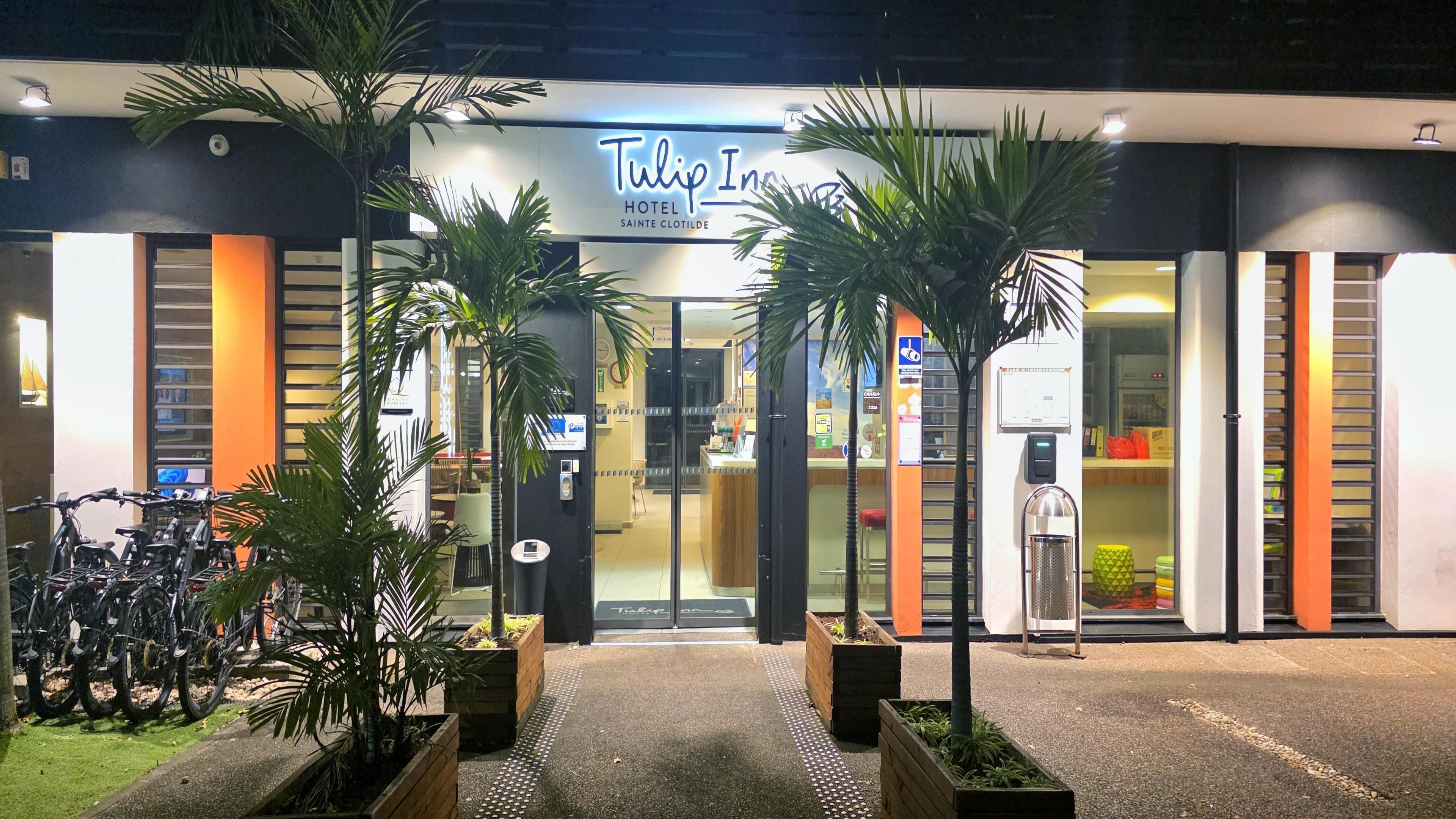 The exterior of Tulip Inn Hotel with a modern design, featuring a prominent entrance, potted plants, and a visible reception area.