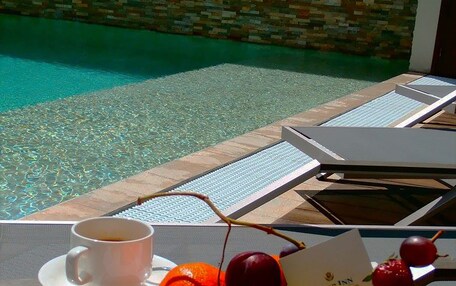 A breakfast setup with croissants, fruit, a glass of orange juice, and a cup of coffee on a table by a poolside.