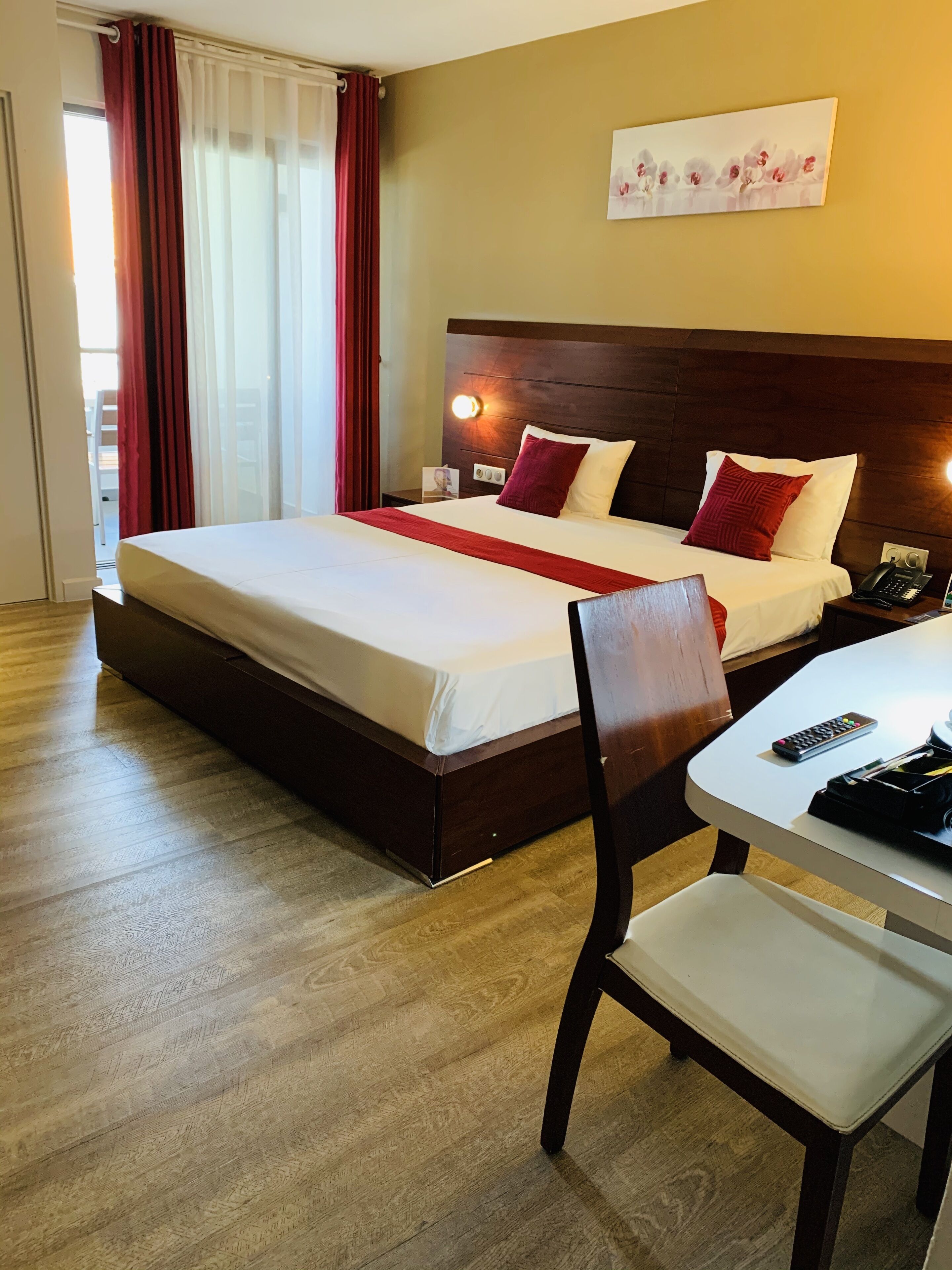 A hotel room with a large bed, a bedside table with a lamp, a chair, and a small table with a remote control.