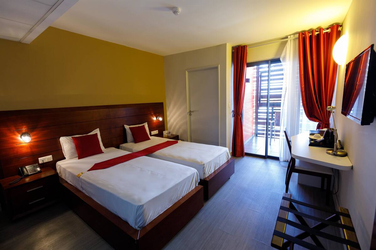 A hotel room with two beds, a desk, a chair, a TV, and a window with curtains.