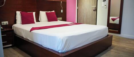 Habitación de hotel con una cama grande, cabecera de madera y pared rosa.