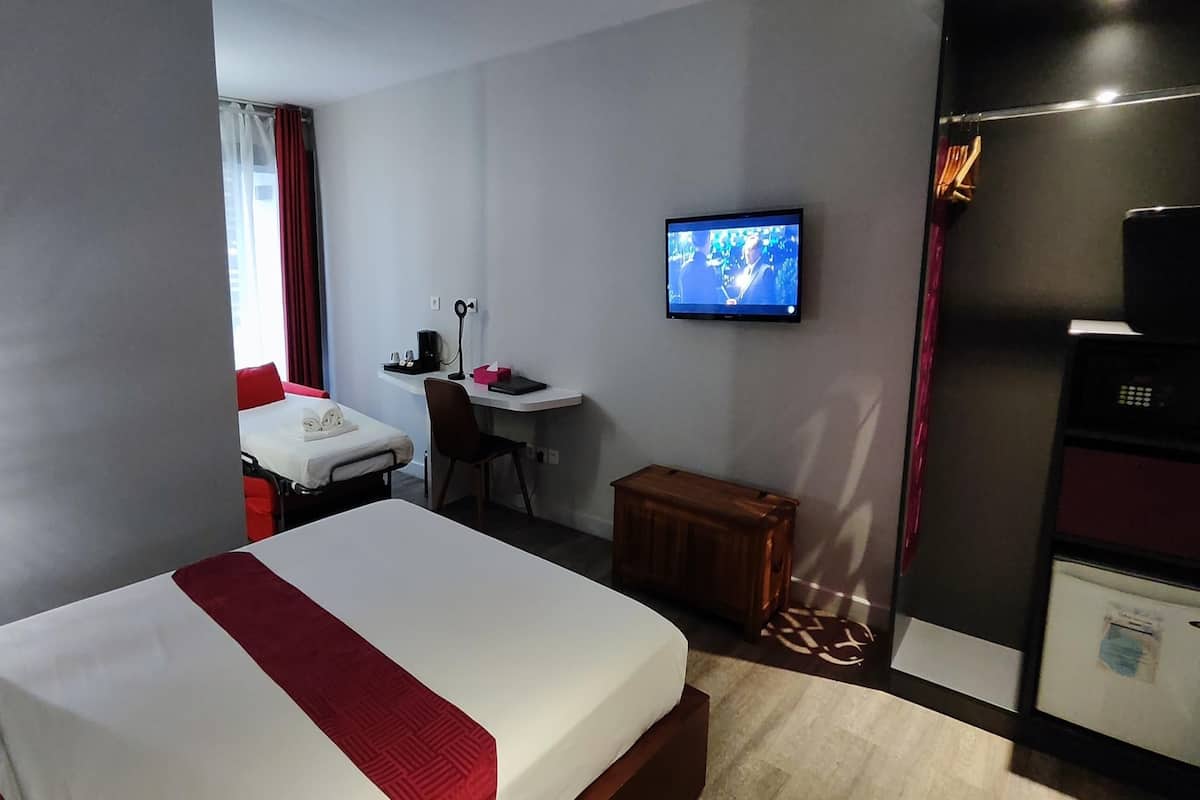 A hotel room with a bed, a desk, a television, and a refrigerator.