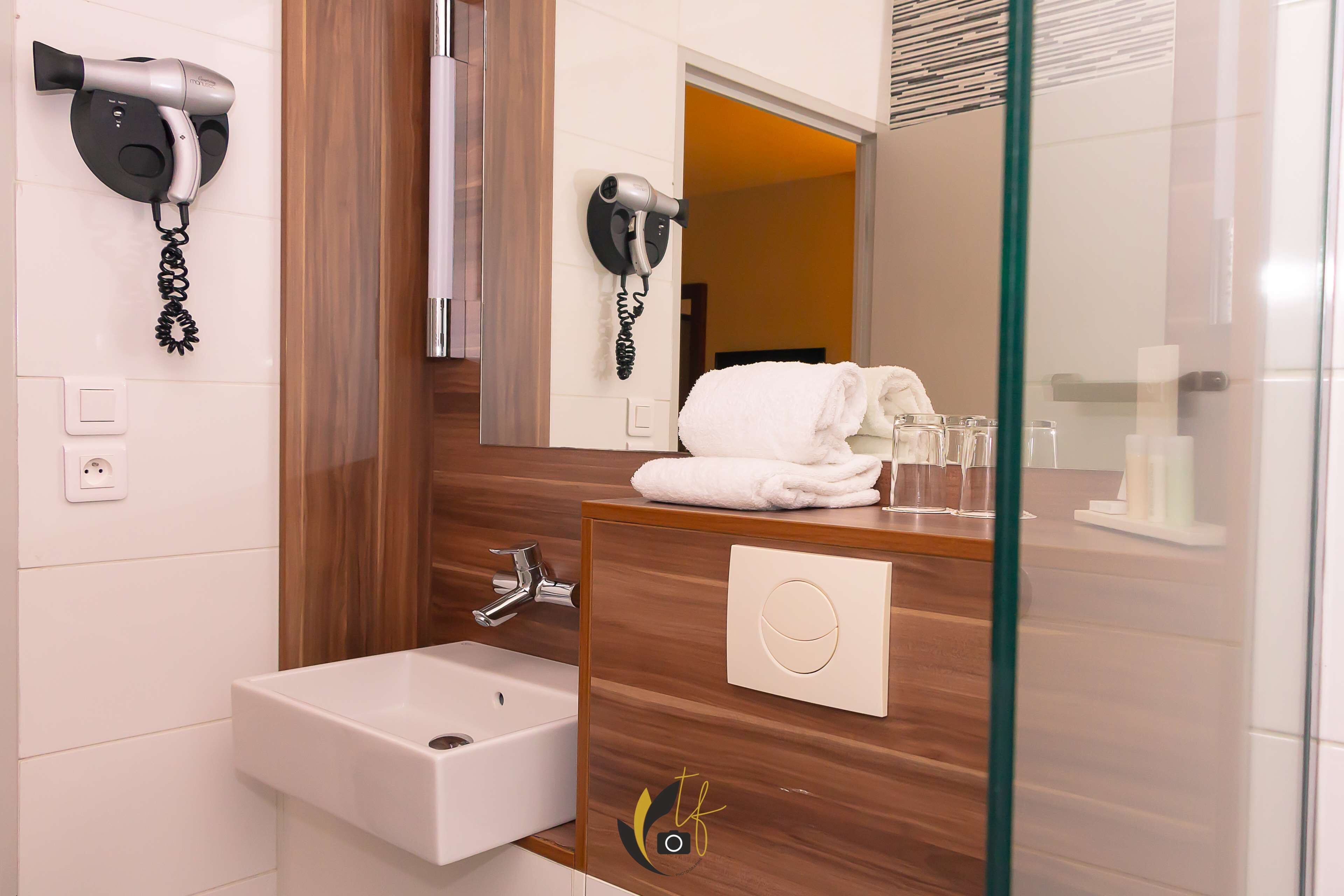 A modern bathroom with a wooden vanity, a white sink, and two hair dryers mounted on the wall.