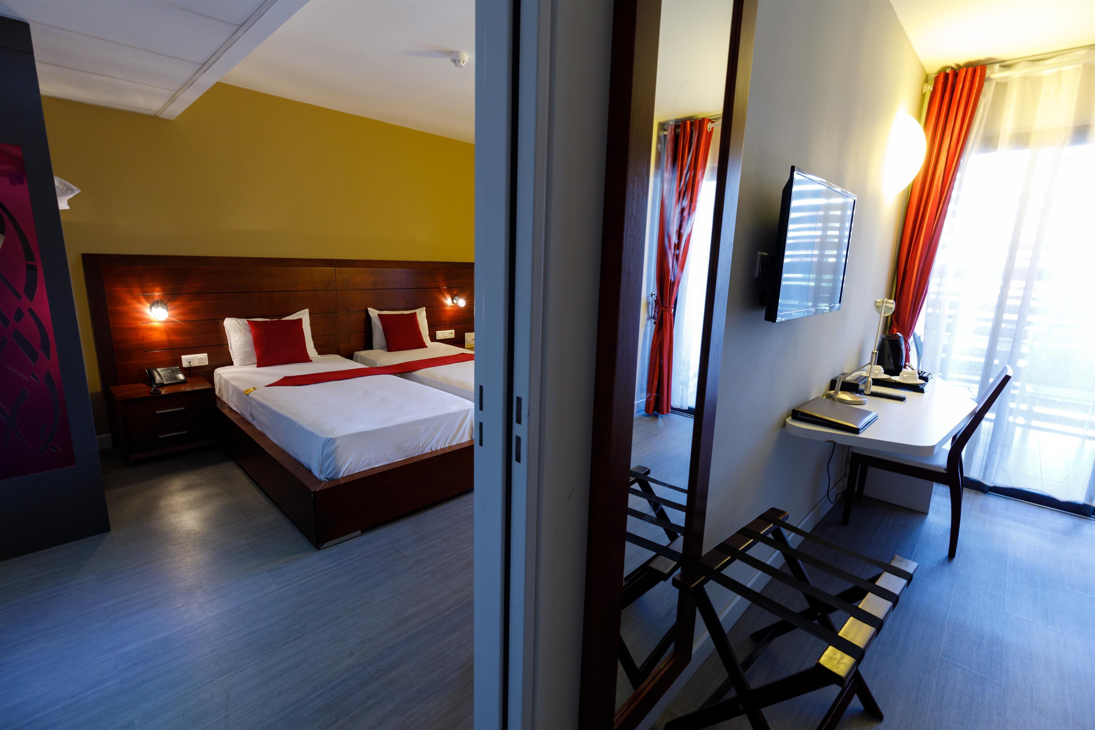 Ein Hotelzimmer mit einem Holzbett, Nachttischlampen, einem Schreibtisch mit Stuhl und einem an der Wand befestigten Fernseher.