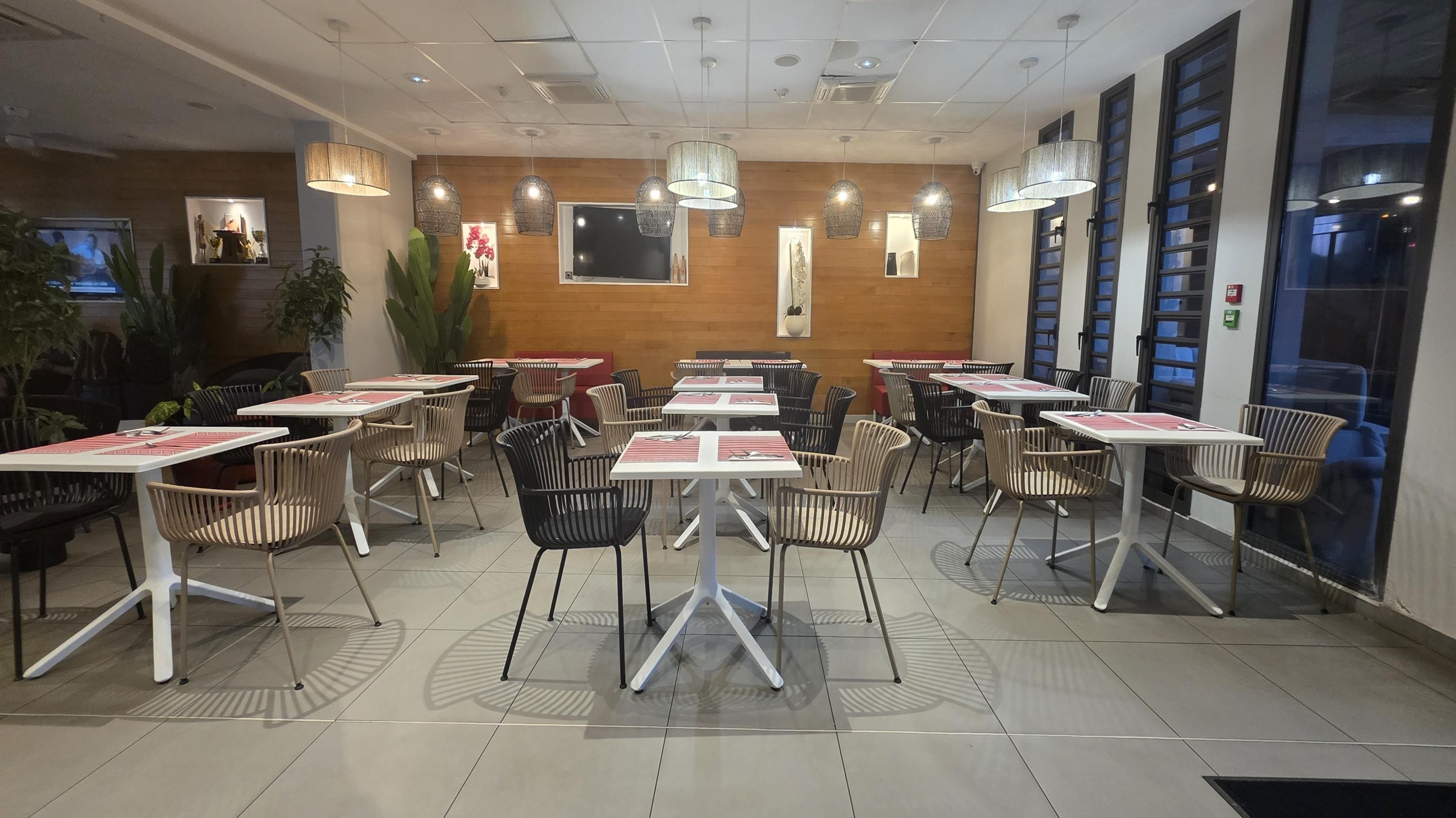 Interior de un restaurante con varias mesas y sillas, luces en el techo y adornos en las paredes.