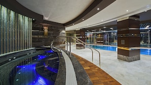 A modern indoor pool area with a glass enclosure, a wooden floor, and a stone wall. - Hilton Istanbul Kozyatagi (Istanbul)