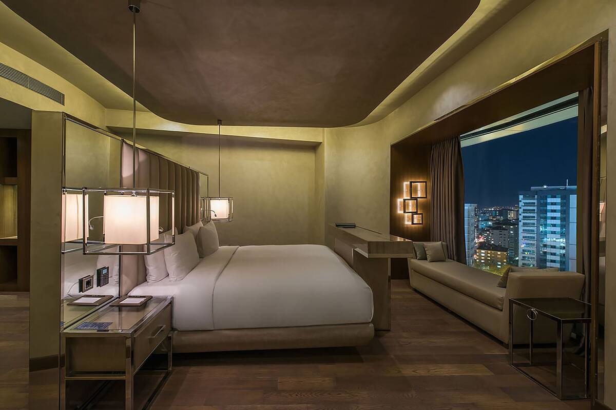 A modern hotel room with a large bed, a desk, a sofa, and a city view.