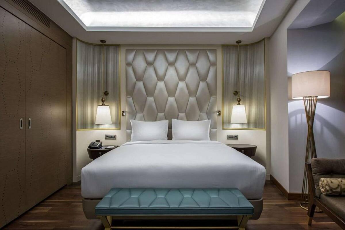 A modern hotel room with a large bed, bedside lamps, a bench, and a skylight.