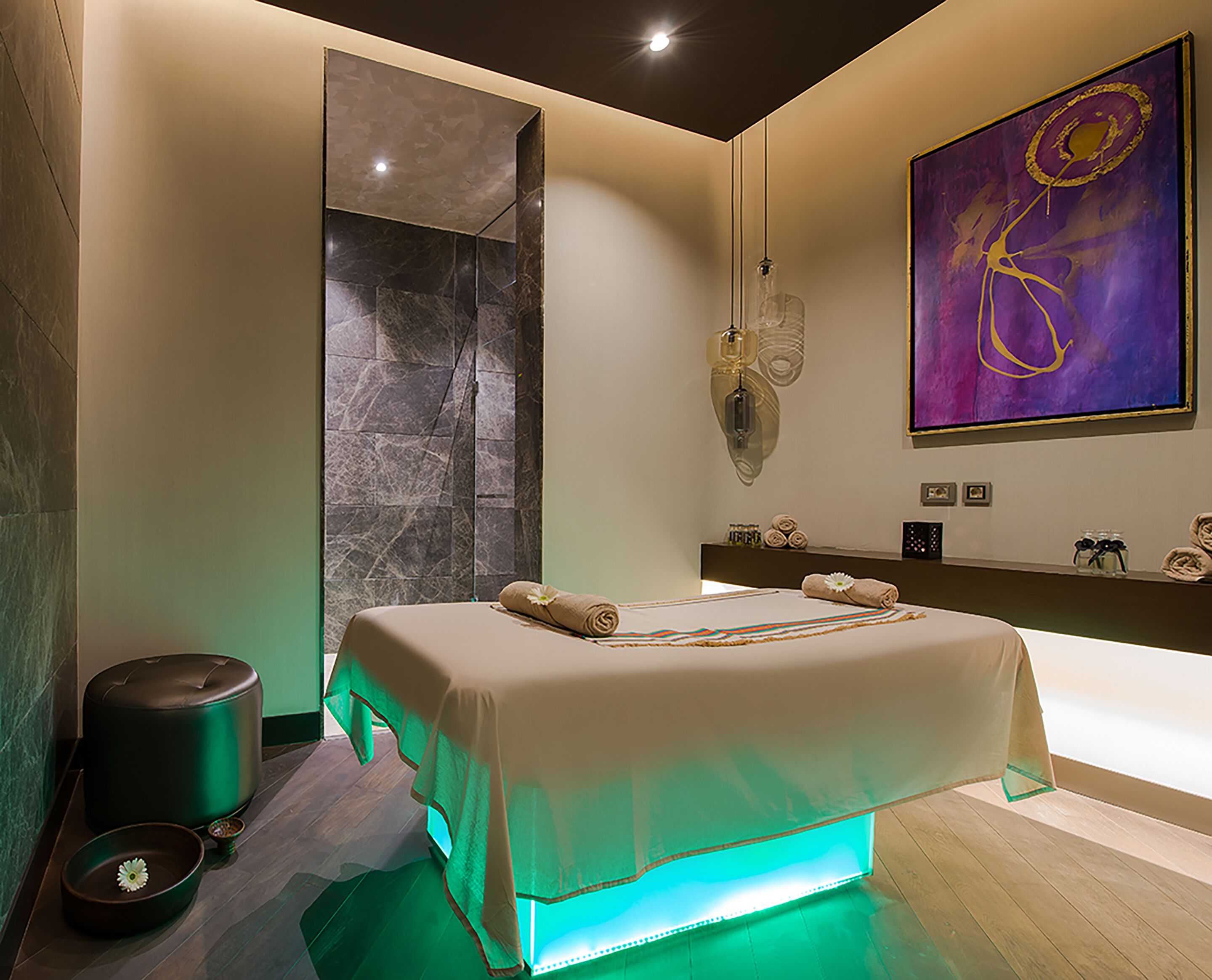 A modern bathroom with a bed, a large mirror, a wall-mounted light fixture, and a painting.