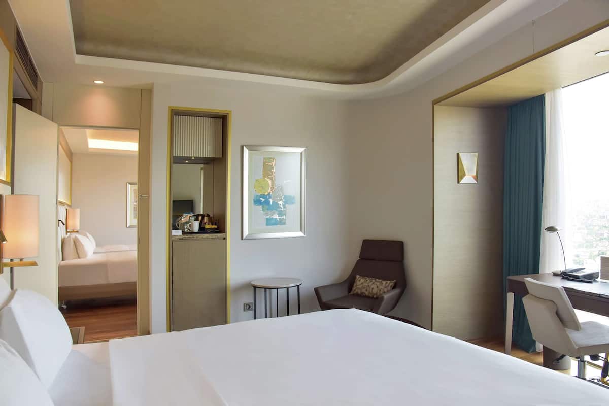 A hotel room with a large bed, a desk, a chair, a small table, and a window with curtains.
