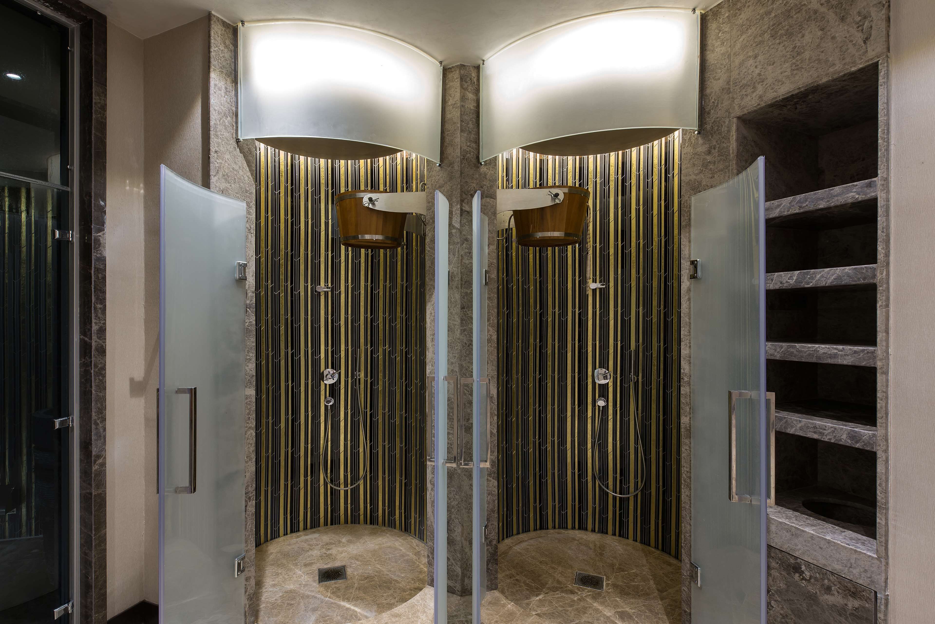 A modern bathroom with two glass-enclosed shower stalls, marble flooring, and vertical striped wall panels.