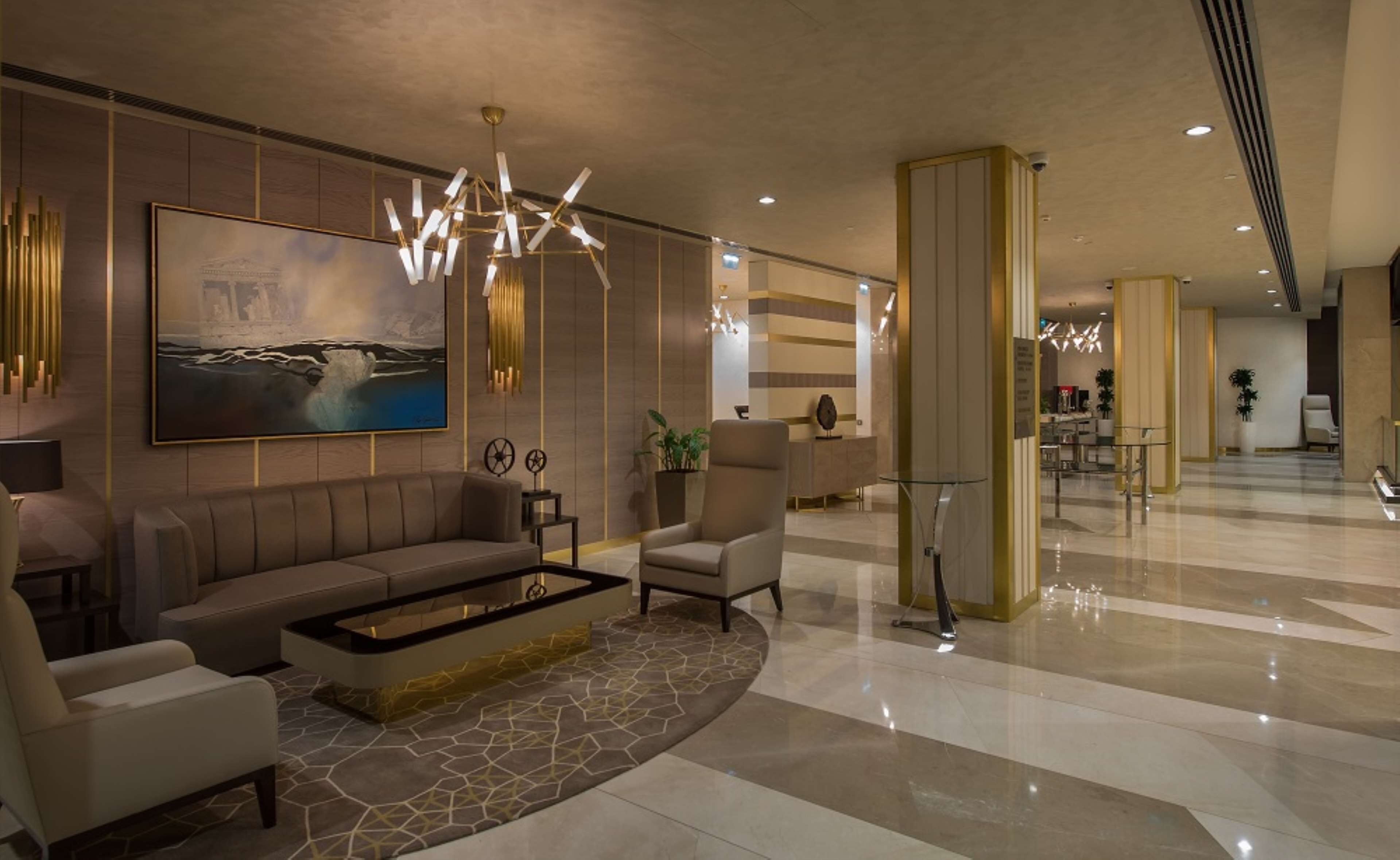 A modern lobby with a sofa, armchairs, a coffee table, a large painting, and a unique chandelier.