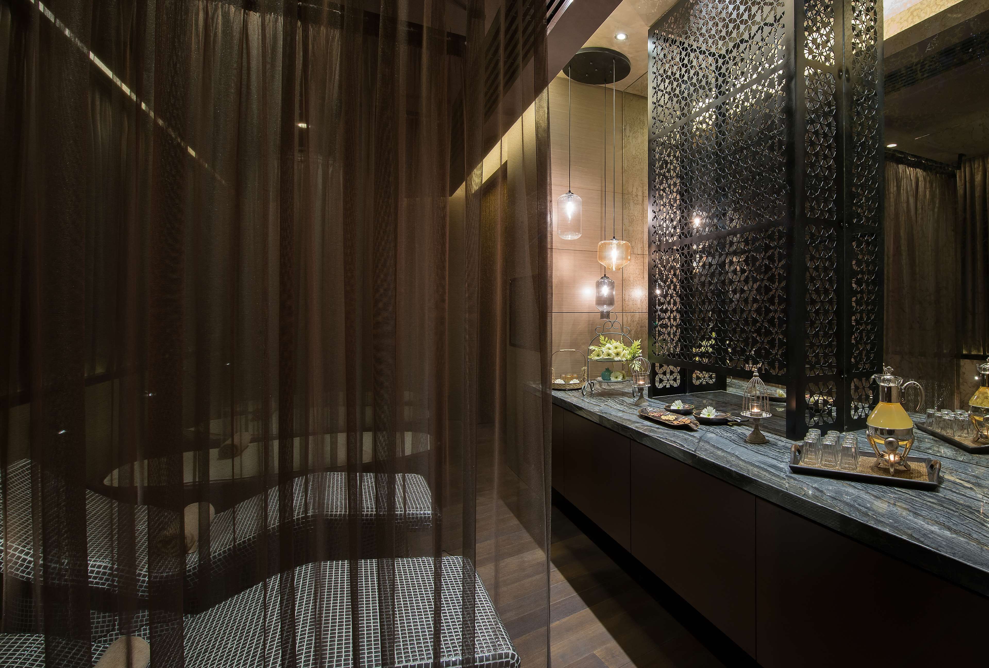 Une salle de bain moderne avec un grand miroir, des rideaux foncés et un comptoir en marbre agrémenté d’objets décoratifs.
