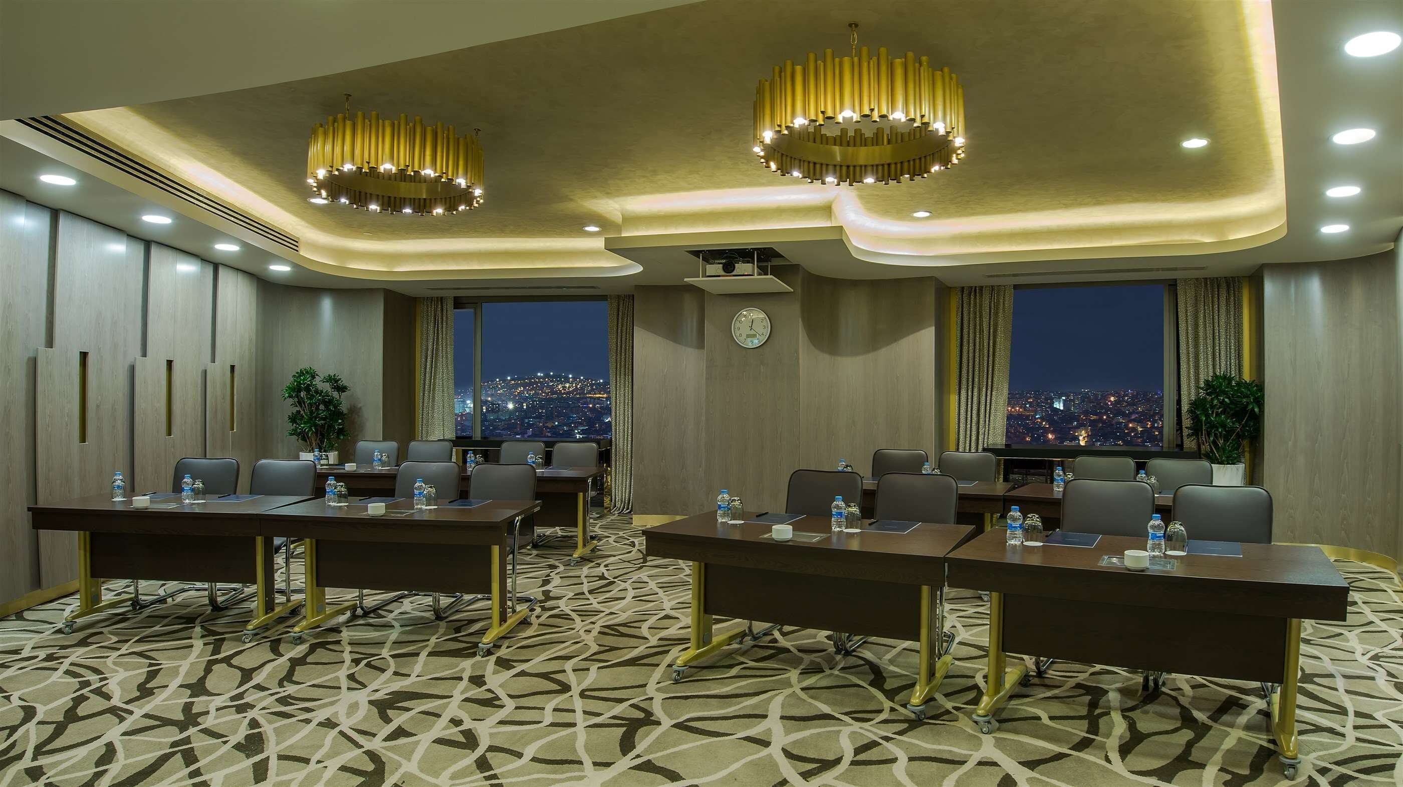 A conference room with two large tables, chairs, a clock, and a city view.