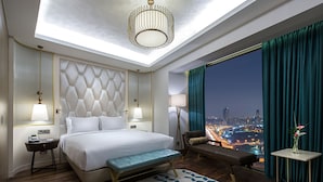 A modern hotel room with a large bed, a bench, a view of the city at night, and a cityscape visible through the window. - Hilton Istanbul Kozyatagi (Istanbul)
