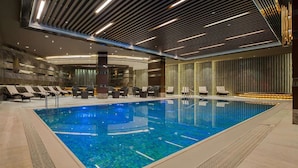 A modern indoor swimming pool with lounge chairs and a contemporary ceiling design. - Hilton Istanbul Kozyatagi (Istanbul)