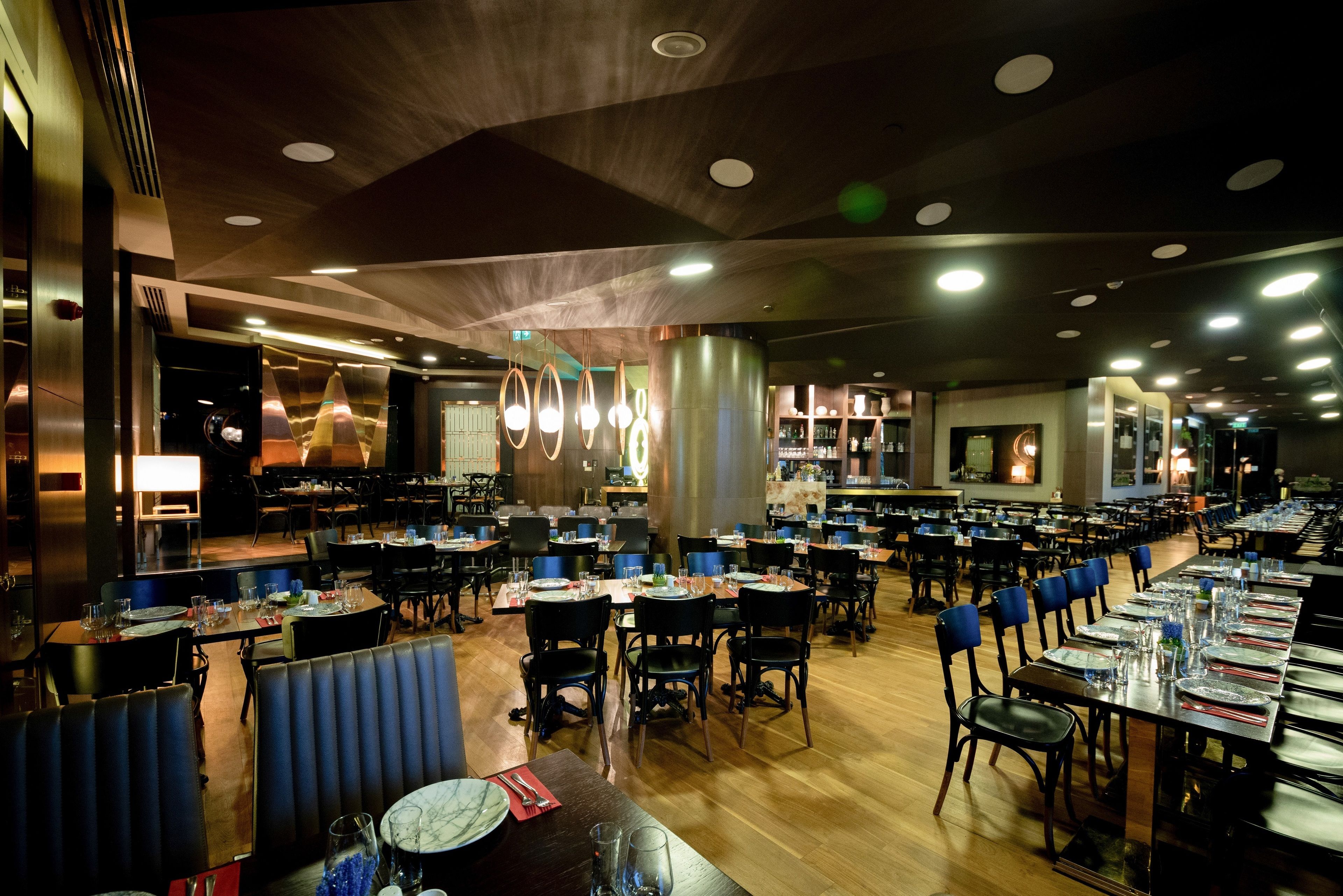 A spacious restaurant with multiple dining tables and chairs, a wooden floor, and a modern ceiling design.