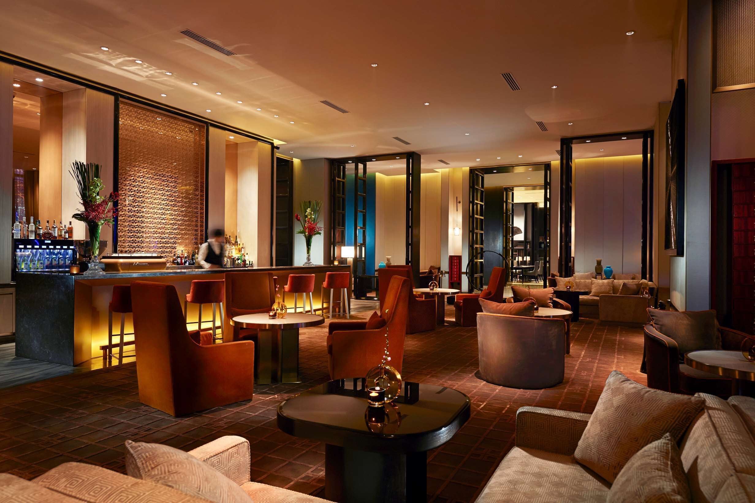 Um hall de hotel moderno com área de bar, assentos e balcão de recepção.