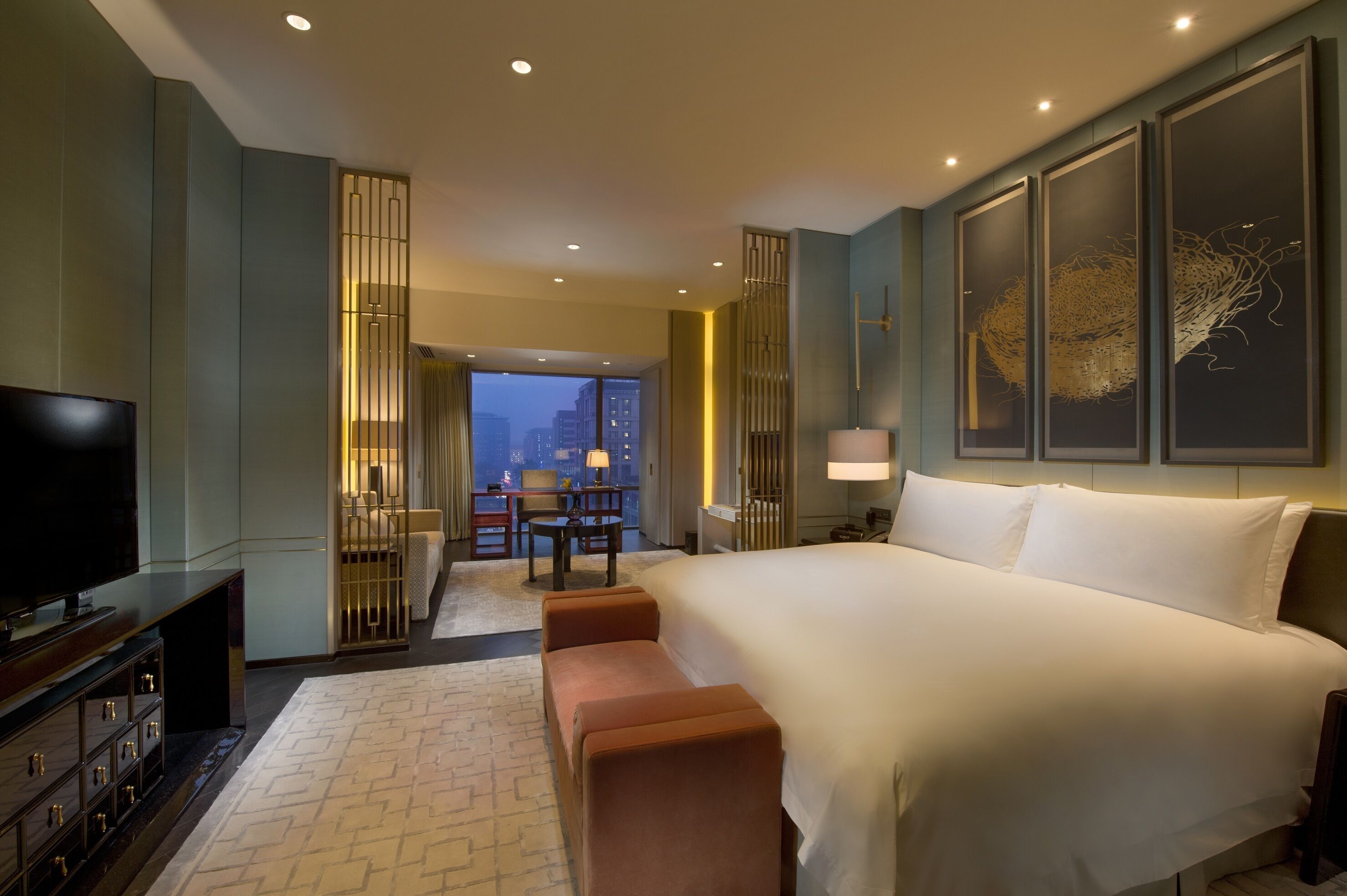 Ein Hotelzimmer mit einem großen Bett, einem Fernseher, einem Schreibtisch und Blick auf die Stadt.