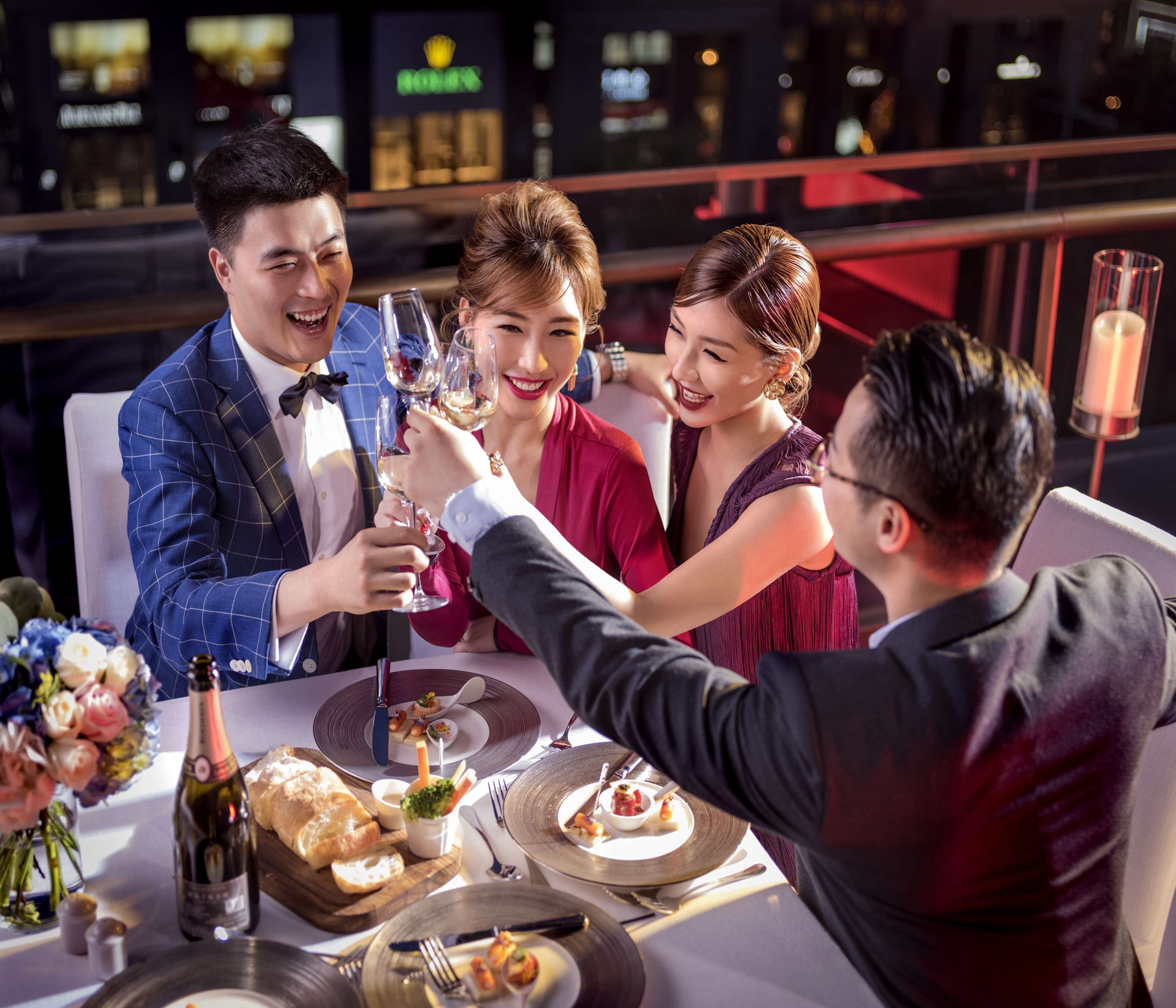 A group of people toasting at a dinner table with various dishes and a bottle of wine.