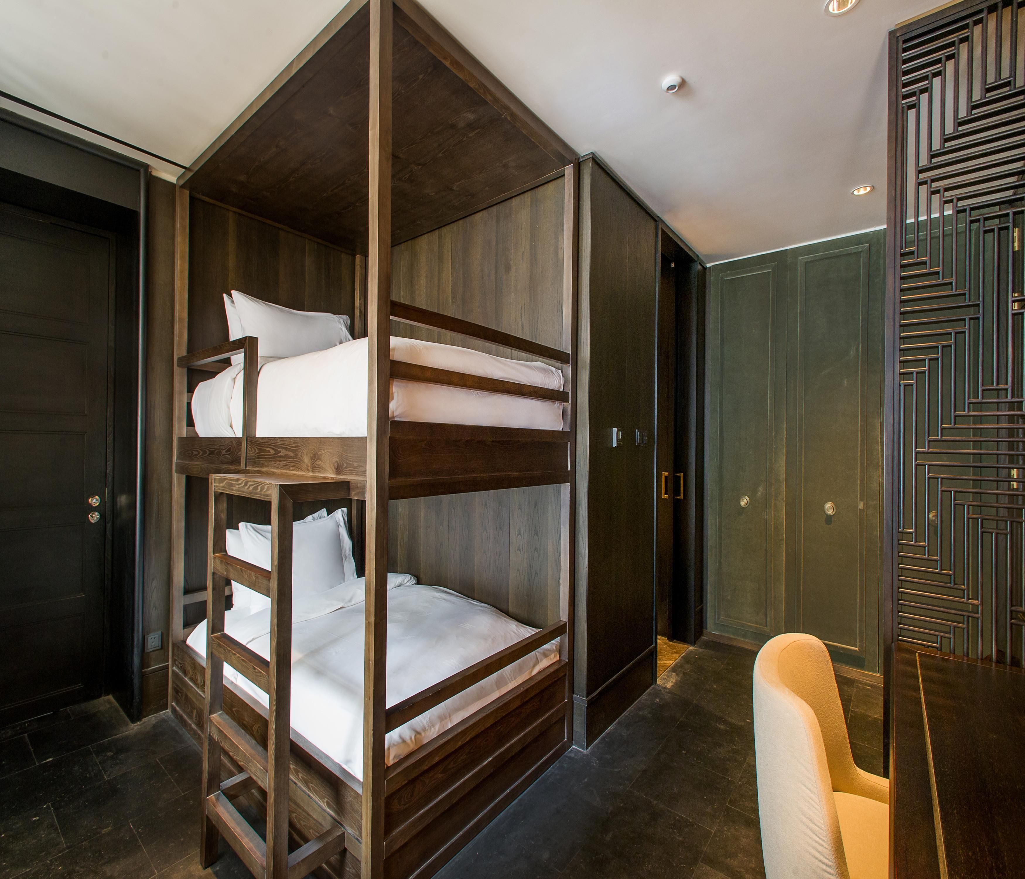 A bunk bed with a wooden frame and white bedding, a dark wooden door, and a patterned wall.