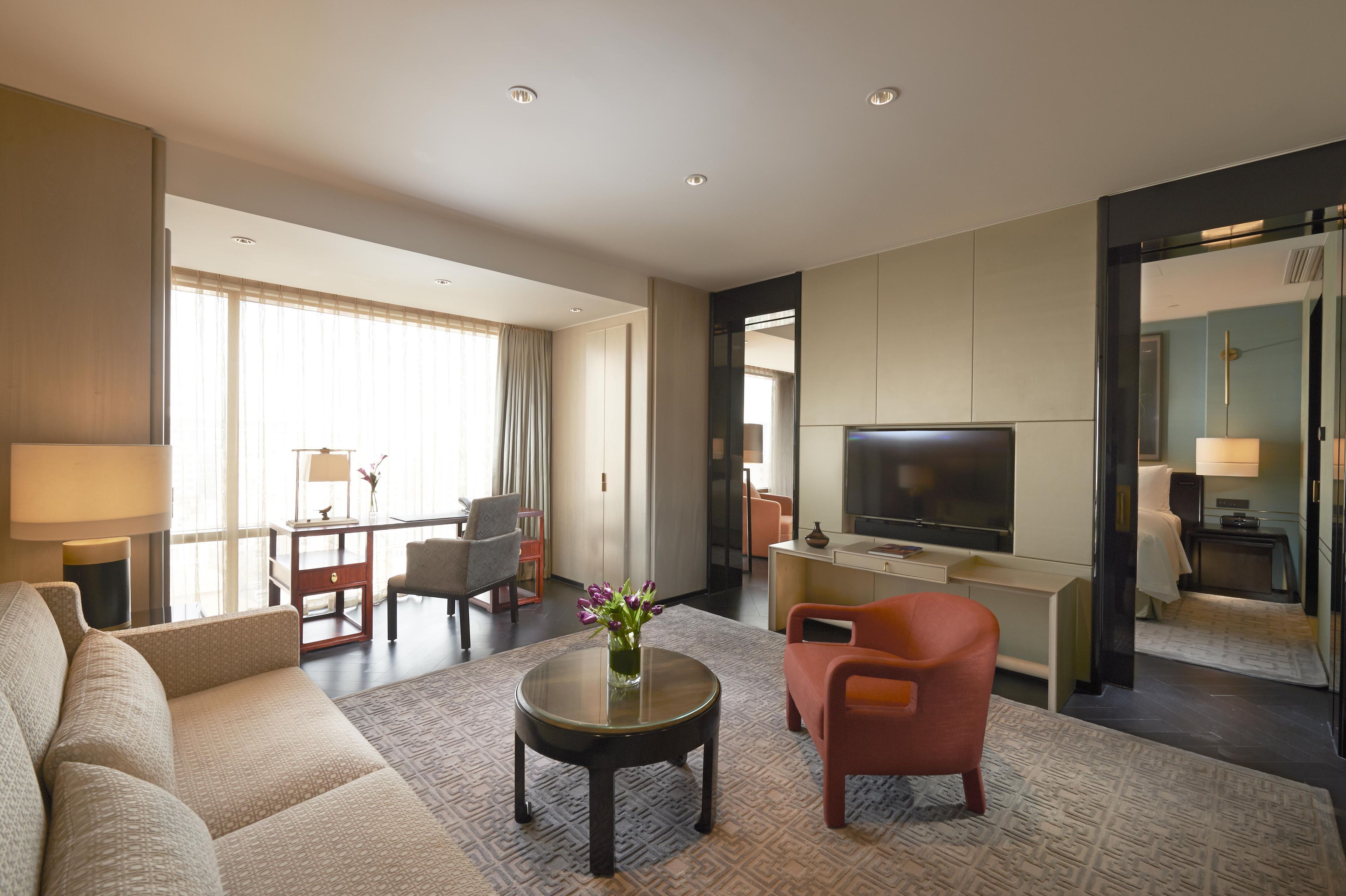 Habitación de hotel con sofá, sillones, una mesa de centro, televisor y escritorio.