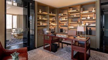 Habitación de hotel moderna con una amplia estantería, un escritorio con lámpara, un sillón de cuero y una alfombra estampada.