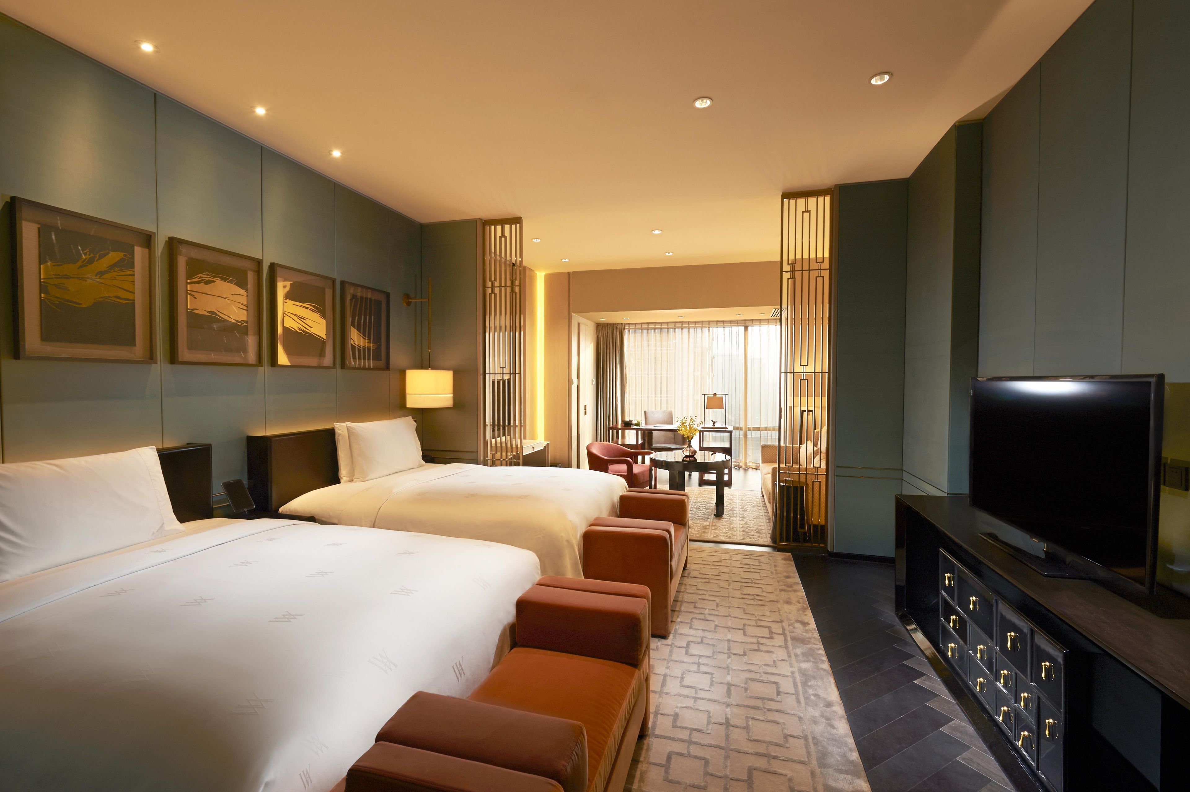 Ein Hotelzimmer mit zwei Betten, einem Fernseher, einem Schreibtisch und Blick auf die Stadt.