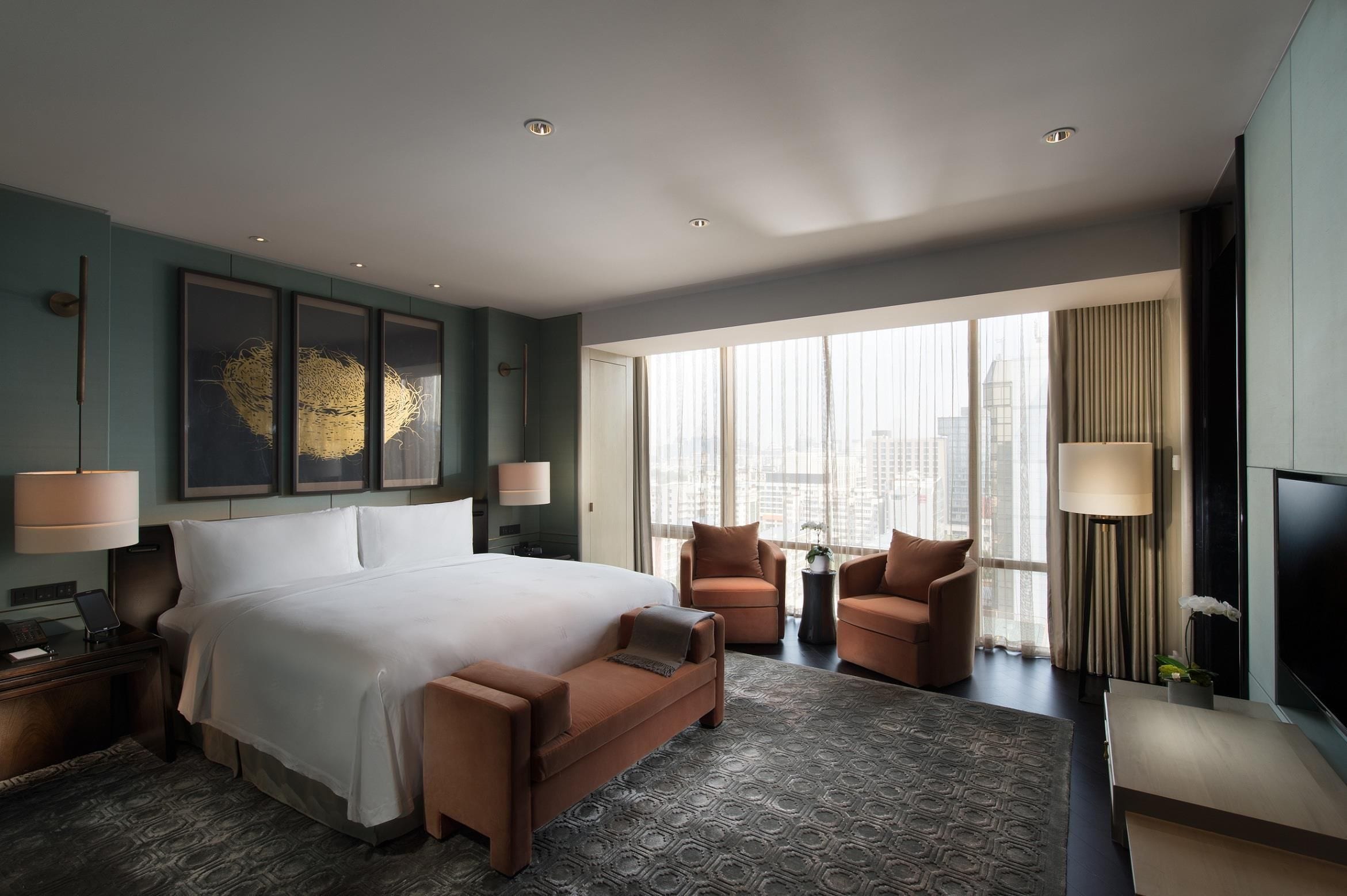 A modern hotel room with a large bed, two armchairs, a small table, and a TV.