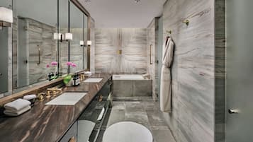 A modern bathroom with a marble wall, a large mirror, a dual sink vanity, a bathtub, and a round rug on the floor.