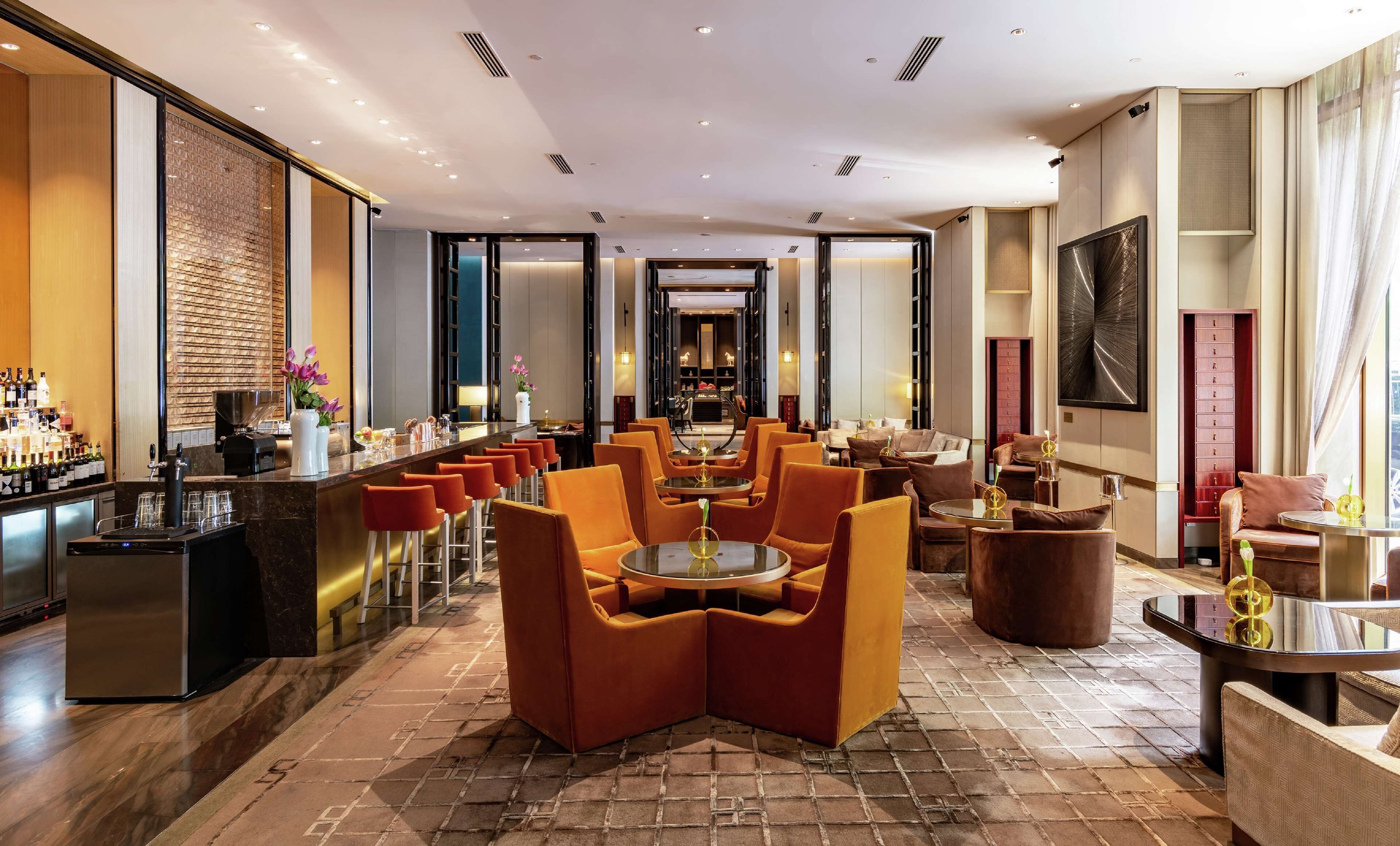 A modern hotel lobby with a bar area, seating arrangements, and a view into the dining area.
