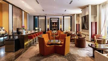 A modern hotel lobby with a bar area, seating arrangements, and a view into the dining area.