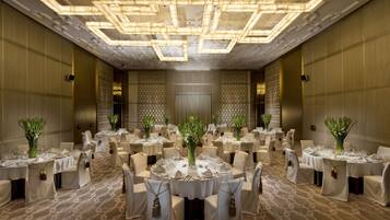 A banquet hall with round tables, chairs, and floral centerpieces.