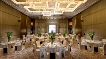 Une salle de banquet avec des tables rondes dressées pour le repas, chacune agrémentée d’un centre de table et recouverte de nappes blanches.