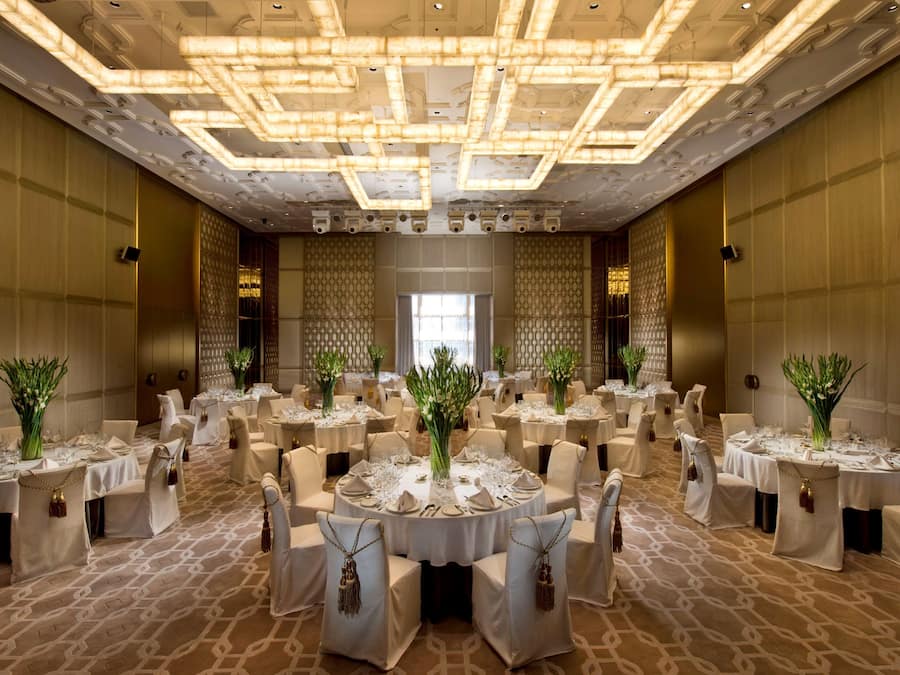 Une salle de banquet avec des tables rondes dressées pour le repas, chacune agrémentée d’un centre de table et recouverte de nappes blanches.