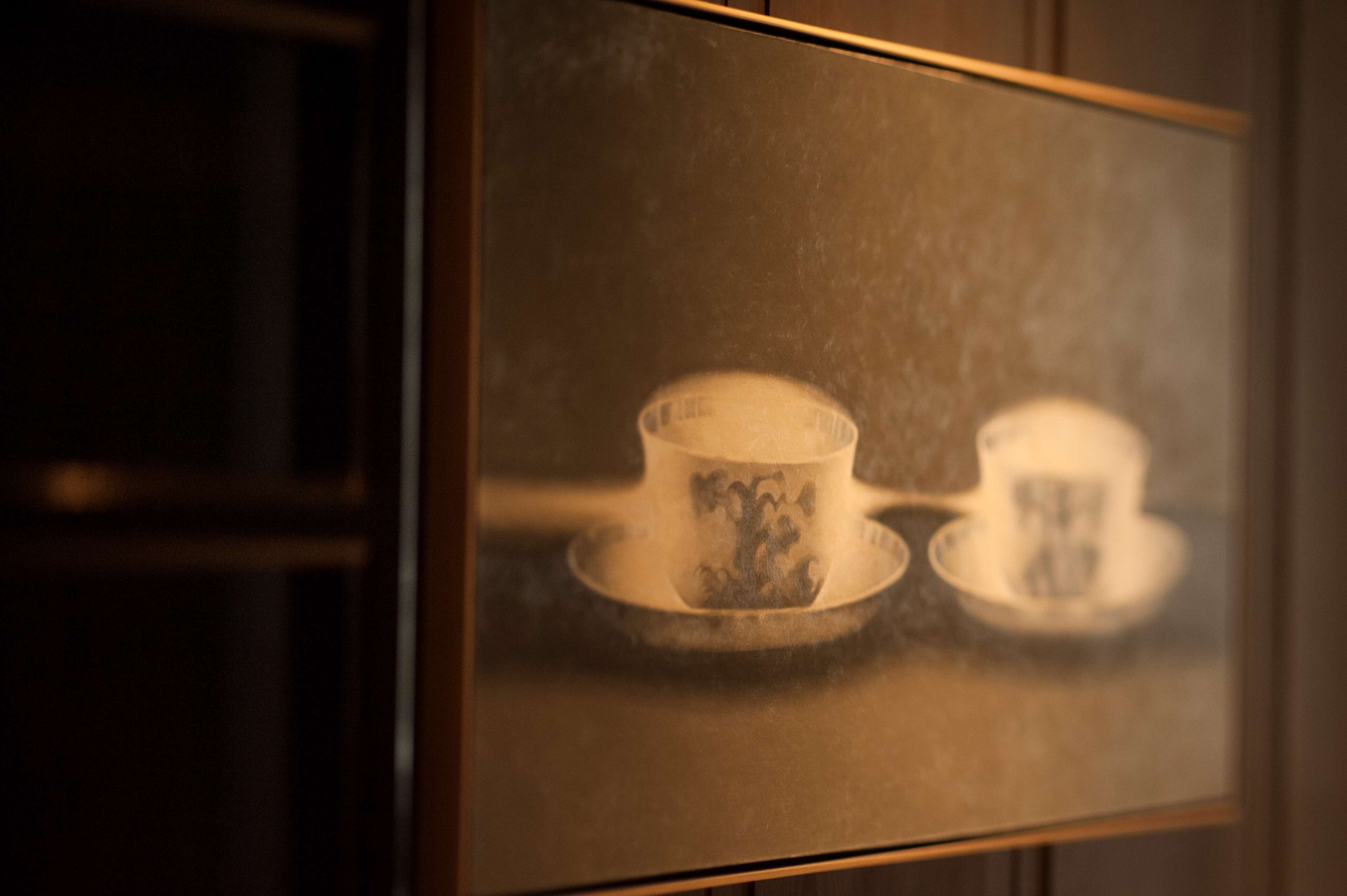 A framed picture of a teacup and saucer on a table.