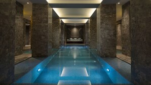 Una piscina interior moderna con una zona de estar central y paredes de piedra.