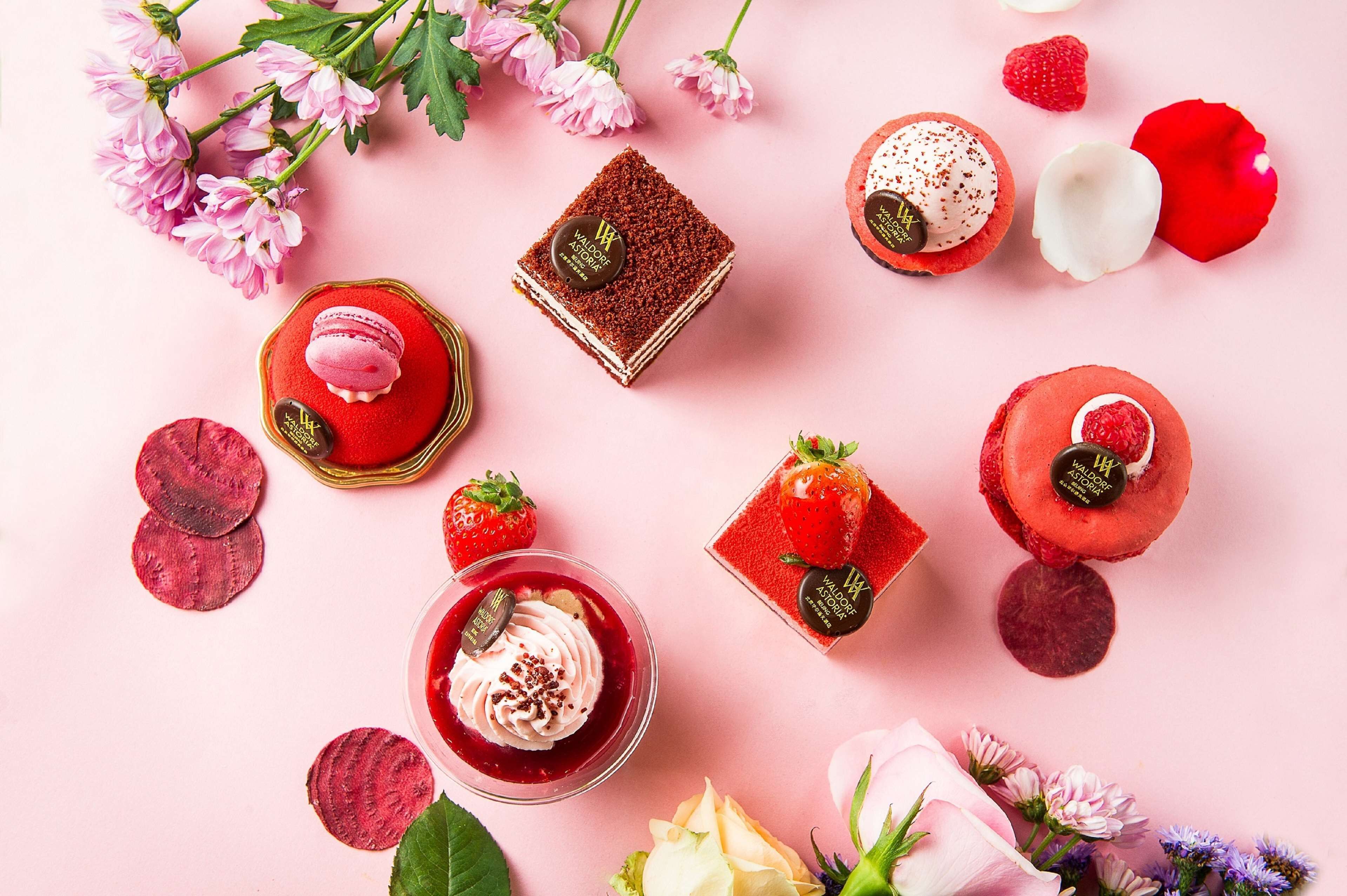 Verschiedene Desserts und Blumen vor einem rosa Hintergrund.