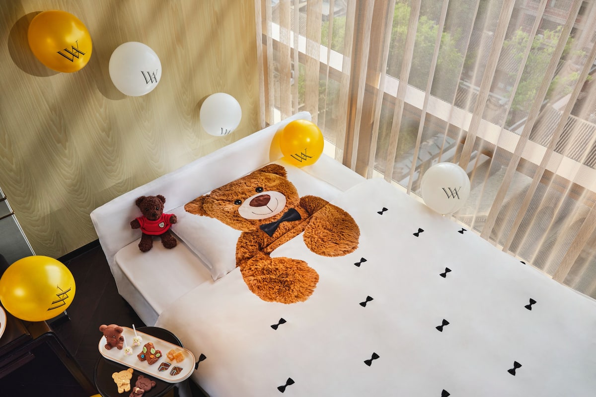A bed with a teddy bear, balloons, and a tray of cookies.