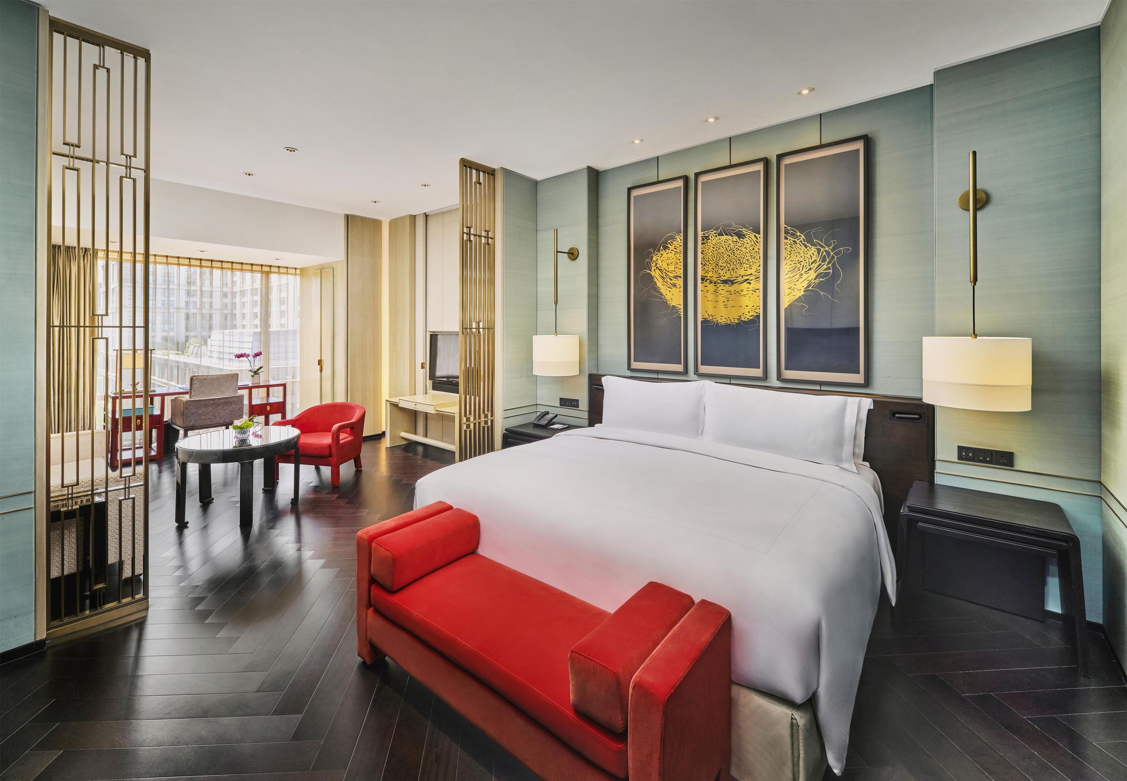 A hotel room with a large bed, a red sofa, a dining table with chairs, and a TV.