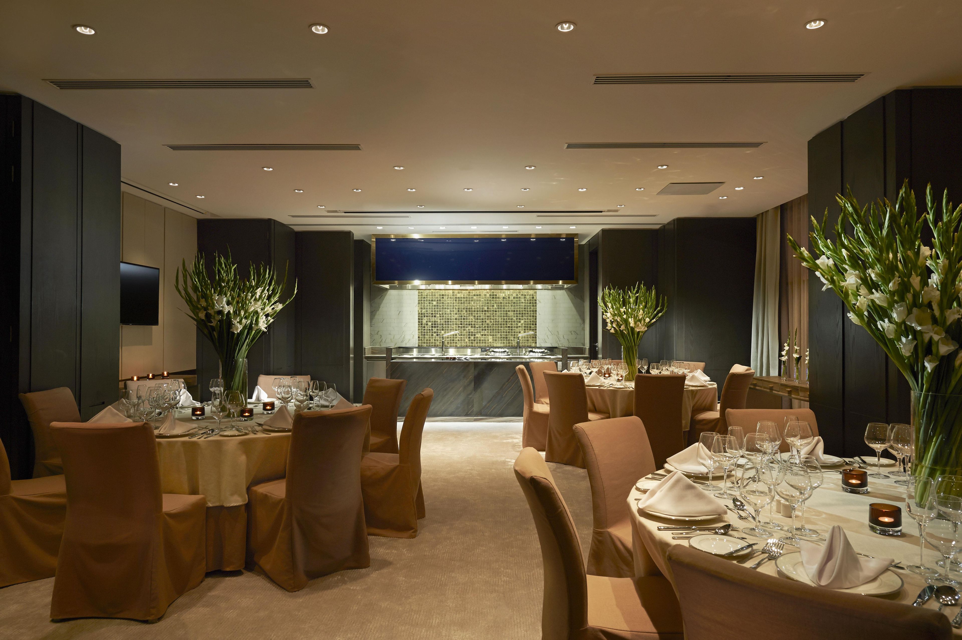 A restaurant with tables set for dining, chairs, and a view of the kitchen.