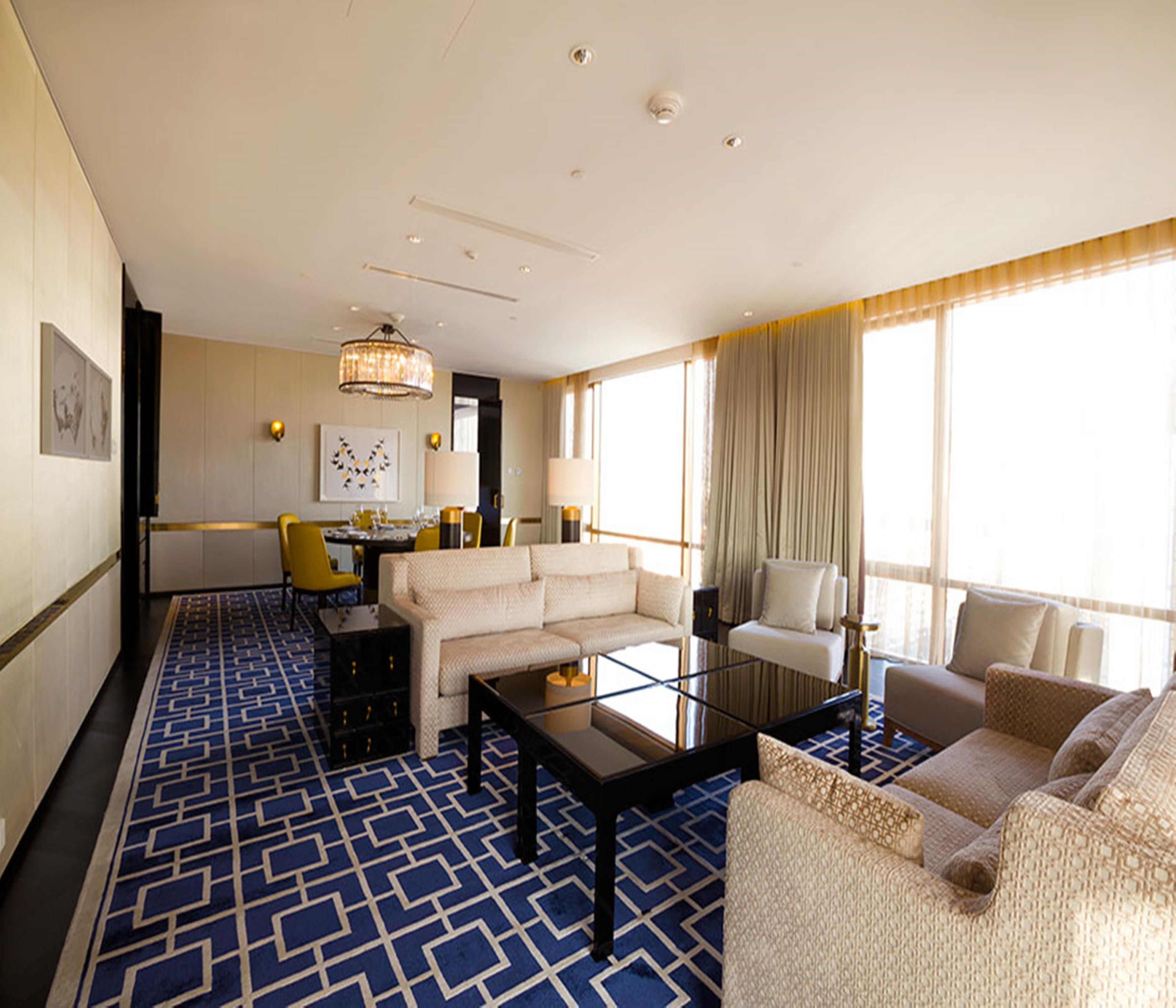 A hotel room with a large window, a sofa, a coffee table, and a dining area with yellow chairs.