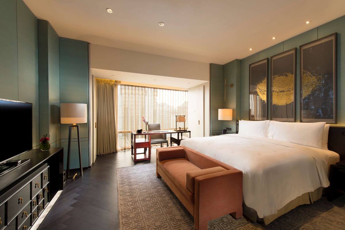 A hotel room with a large bed, a television, a desk with a chair, and a sofa.