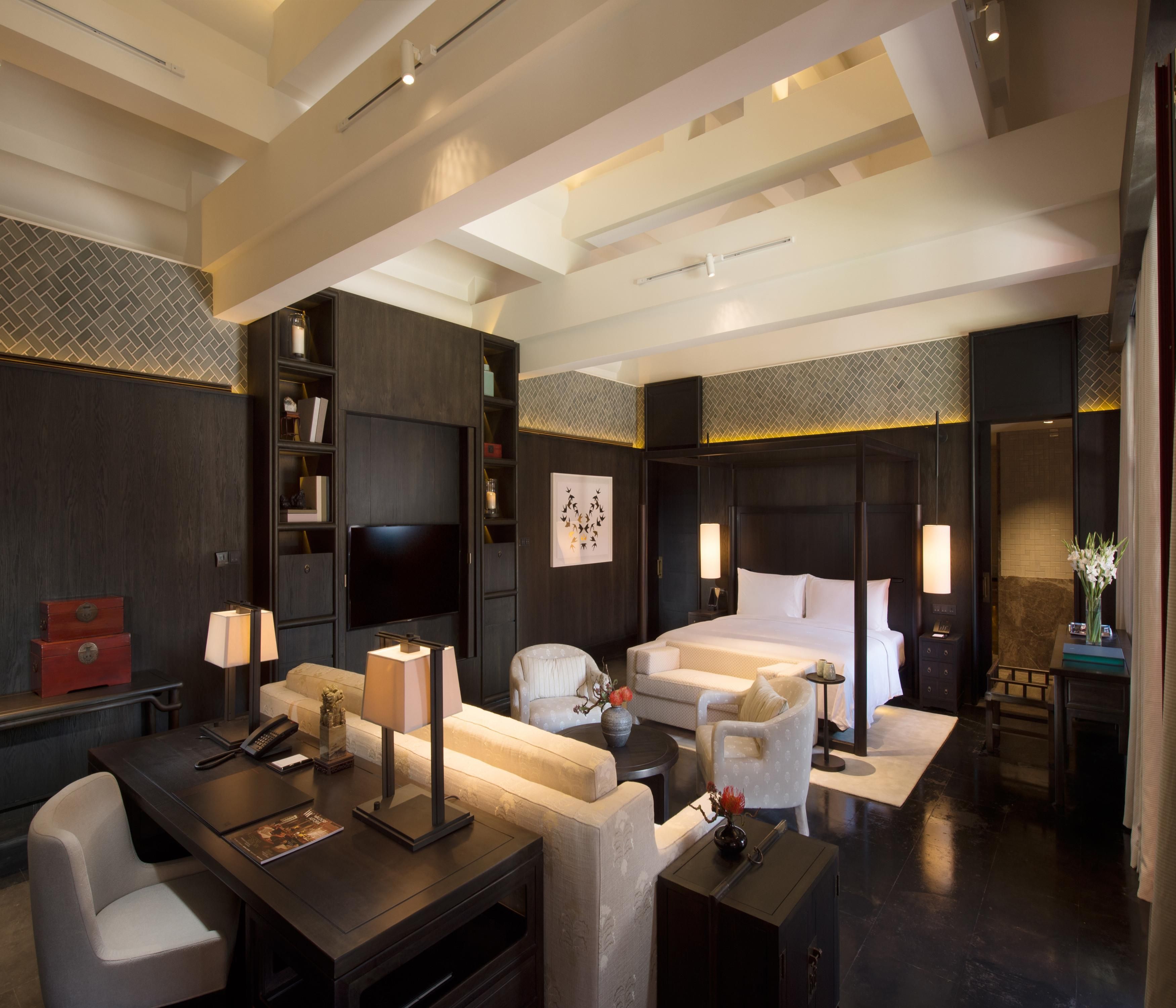 Une chambre d’hôtel moderne dotée d’un grand lit, d’une télévision, d’un bureau avec une lampe et d’un coin salon comprenant un canapé et des fauteuils.
