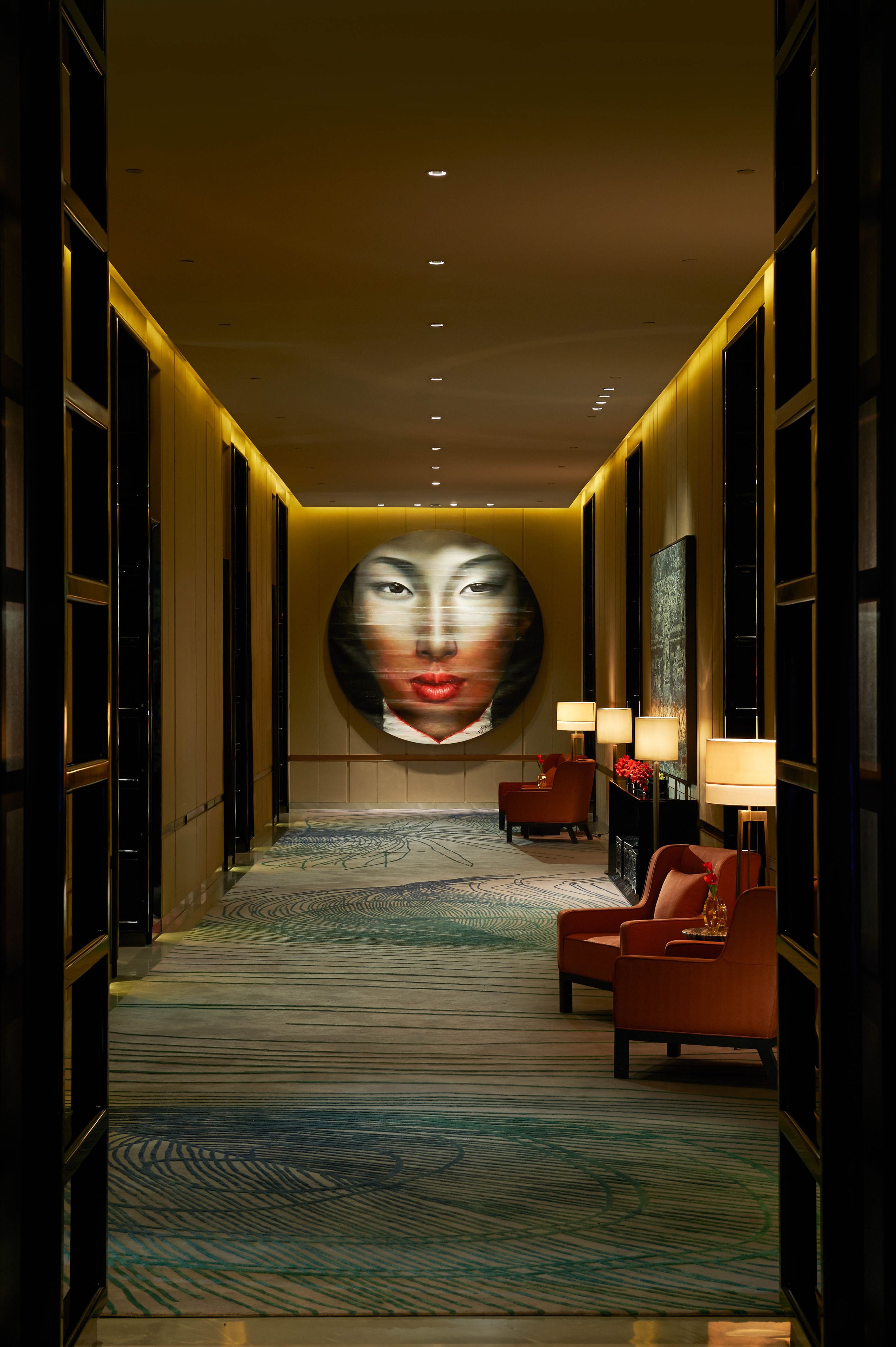 A hallway with a patterned carpet, red armchairs, and a large abstract painting on the wall.