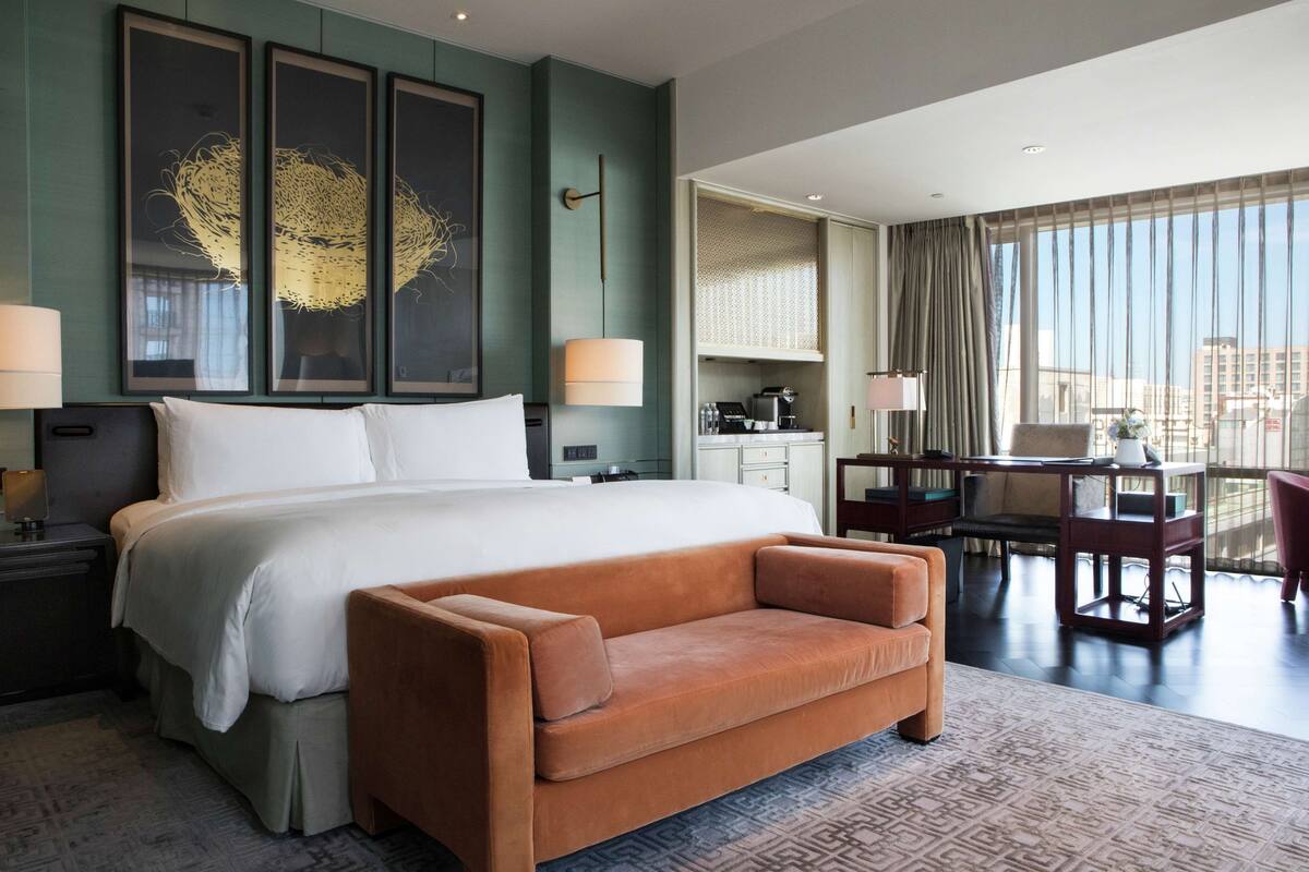 A hotel room with a large bed, a sofa, a desk, and a view of the city.