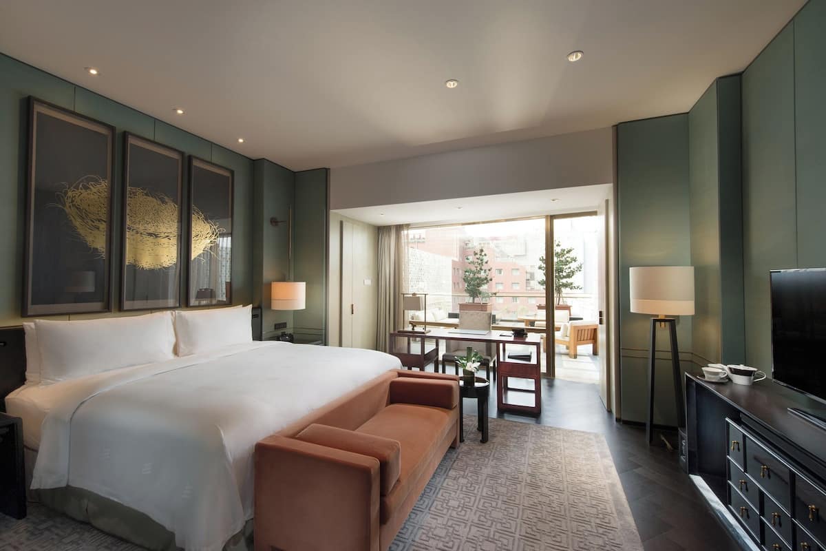 A hotel room with a large bed, a sofa, a TV, and a dining area with a table and chairs.