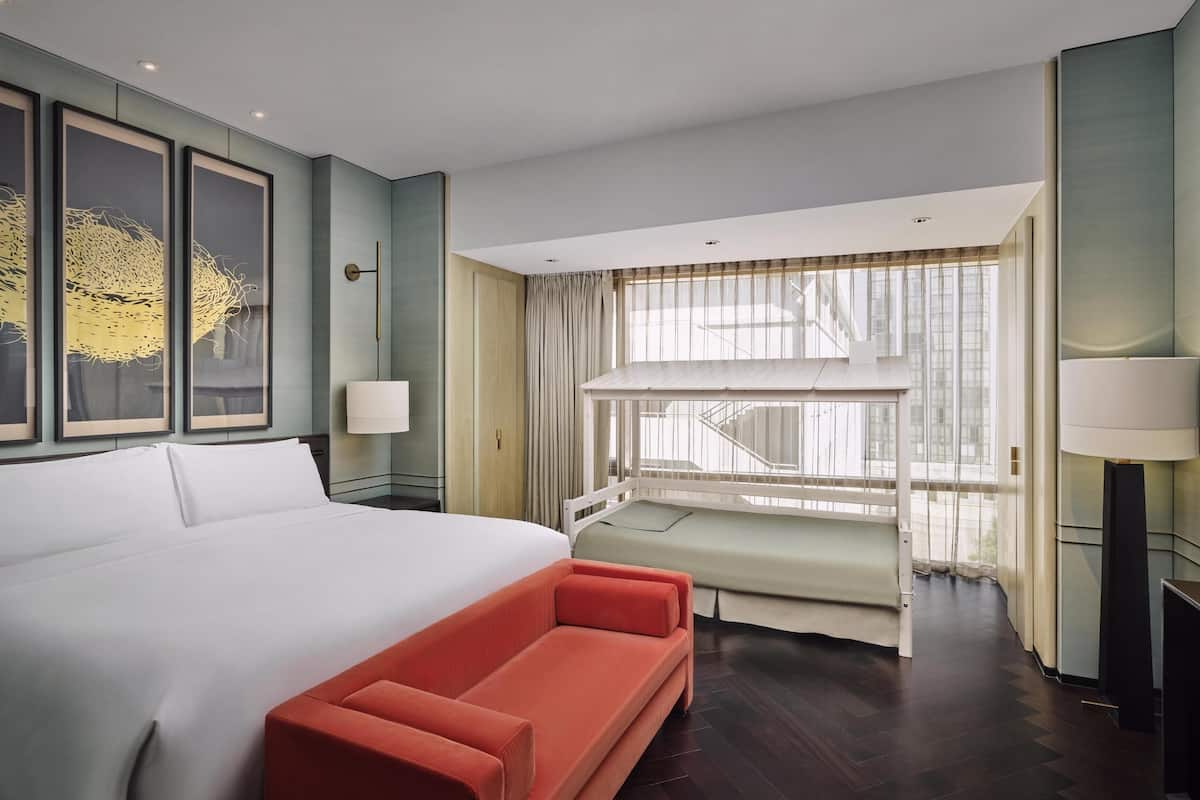 A hotel room with a large bed, a red sofa, a window with a view of a building, and a staircase.